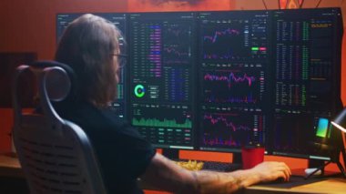 Erkek tüccar, gerçek zamanlı hisse senetlerini izler ve analiz eder. Çoklu monitörlü bilgisayar çalışma istasyonunda borsa grafiklerini değiştirir. Adam akşamları merkez büroda uzaktan yatırım işinde çalışıyor. Kripto para ticareti.