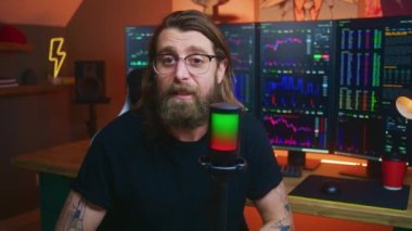 Adam mikrofon kullanarak konuşuyor, şifreli para ticareti veya yatırım hakkında blog için eğitici video dersini kaydediyor. Gerçek zamanlı hisse senetleri, döviz borsaları olan çoklu monitörlü bilgisayar..