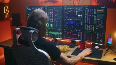 Erkek tüccarın gerçek zamanlı hisse senetlerini analiz ederken, çoklu monitörlü bilgisayar çalışma istasyonunda borsa grafiklerini değiştirirken, fast food yerken. Adam iç işlerinde yatırım yapıyor. Kripto para ticareti.