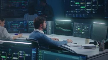 Yazılım mühendisi izleme odasındaki bilgisayarda çalışıyor. Teknik destek sunucu verilerini gece geç saatlerde analiz eder. Duvarda gerçek zamanlı analiz çizelgeleri olan çok sayıda büyük ekran var. Siber güvenlik.