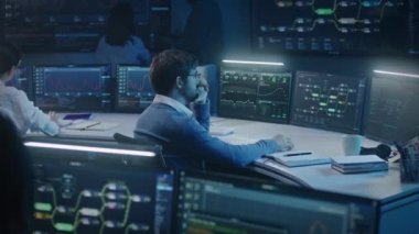 Yazılım mühendisi gece geç saatlerde izleme odasında bilgisayar başında çalışıyor. Büyük veri bilimcileri sunucu verilerini analiz eder. Duvarda gerçek zamanlı analiz çizelgeleri olan çok sayıda büyük ekran var. Siber güvenlik.