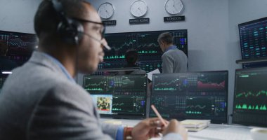 Mali analistlerden oluşan ekip, birçok büyük ekranda döviz piyasası grafiklerini analiz ediyor. Gerçek zamanlı sergilenen hisse senetleriyle bilgisayar başında çalışan Afro-Amerikan bir adamı vurdu. Ticaret ve yatırım..