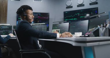 Afro-Amerikalı tüccar gerçek zamanlı sergilenen hisselerle bilgisayar başında notlar alır ve çalışır. Meslektaşlar, arka plandaki büyük ekranlardaki döviz piyasalarının grafiklerini analiz ederler. Kripto para birimi ticareti ve yatırımı