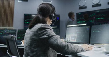 Elinde kalemle bilgisayar başında gerçek zamanlı hisse senedi sergileyen kadın bir finans analisti. Meslektaşlar, arka plandaki büyük ekranlardaki döviz piyasalarının grafiklerini analiz ederler. Ticaret ve yatırım kavramı.