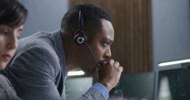 Çok ırklı finansal analistler gerçek zamanlı hisse senetleri ve banka ofisindeki borsa grafikleriyle bilgisayar üzerinde çalışıyorlar. Televizyon haberleri büyük dijital ekranda yayınlanıyor. Kripto para ticareti ve analitik. Kapat.