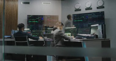 Çok ırklı finansal analistler gerçek zamanlı sergilenen çoklu monitörlü bilgisayarlar üzerinde çalışıyorlar. Meslektaşlar büyük ekranlarda döviz piyasalarının grafiklerini analiz ederler. Kripto para ticareti kavramı.