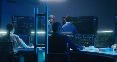 Bilgi işlem uzmanları ve yazılım programcılarından oluşan çok ırklı bir ekip, veri sunucusu, analiz çizelgeleri ve bilgisayarlardaki engelleme ağı ve geceleri izleme ofisindeki büyük dijital ekranlar üzerinde çalışıyor..