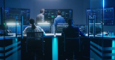 Bilgi işlem uzmanları ve yazılım programcılarından oluşan çok ırklı bir ekip, veri sunucusu, analiz çizelgeleri ve bilgisayarlardaki engelleme ağı ve geceleri izleme ofisindeki büyük dijital ekranlar üzerinde çalışıyor..