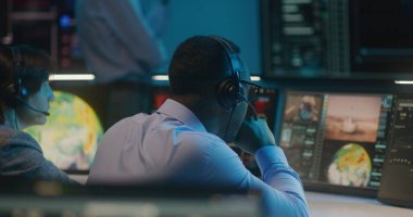 Kulaklık takmış çeşitli uçuş kontrol çalışanları görev kontrol merkezindeki bilgisayarlardan uzay görevlerini izliyorlar. Ekip, büyük dijital ekranlarda gösterilen başarılı uzay roketinin fırlatılmasından sonra el çırpıyor.