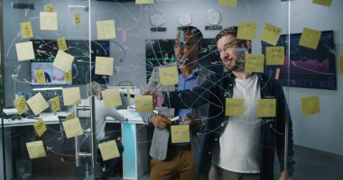 Afrika kökenli Amerikalı finans analisti ve yatırım yöneticisi cam duvara resim çiziyor, banka ofisinde iş yatırımları stratejisini tartışıyor ve geliştiriyor. Döviz piyasası grafikli bilgisayarlar ve dijital ekranlar