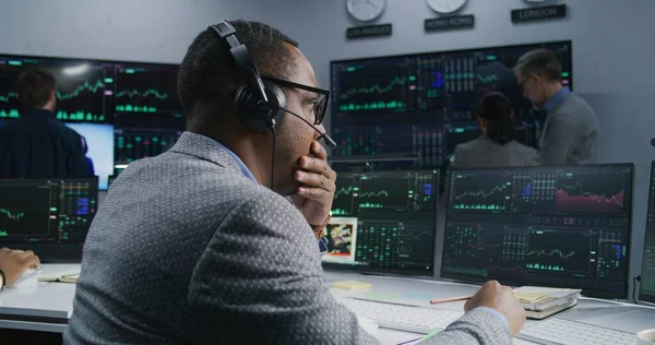 手握钢笔的非洲裔美国投资者在电脑上工作 拥有实时股票 同事们在大屏风的背景下分析外汇市场图表 贸易和投资的概念 — 图库照片