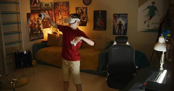 Vrヘッドセットの少年は ワイヤレスコントローラを使用して拡張現実オンラインビデオゲームをプレイし 夜に寝室で余暇時間を過ごします 現代的なデバイス エンターテイメント ライフスタイルの概念 — ストック写真