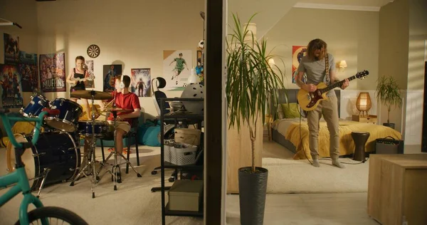 Man plays guitar in bedroom. Young boy plays drum kit and young girl plays ukulele, jumps on bed. View of two rooms or apartments separated by wall. Concept of music, neighbourhood and lifestyle.