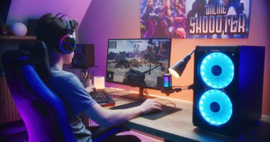 Genç oyuncu evdeki bilgisayarda oyun oynarken tankı kontrol ediyor. Bilgisayar monitörü çevrimiçi video oyunu canlı yayını ya da siber spor turnuvasıyla. Masa, RGB LED lambasıyla aydınlatılmış. Arka plan.