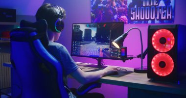 Kulaklıklı genç oyuncu bilgisayarda birinci şahıs nişancıyla oynuyor. Çevrimiçi video oyunu canlı yayın ya da esports turnuvası. Masa, RGB LED lambasıyla aydınlatılmış. Ev konseptiyle oynamak. Arka plan.