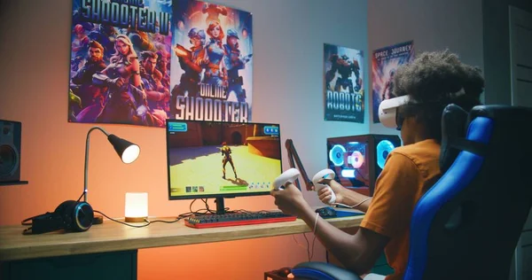 Vrヘッドセットのアフリカ系アメリカ人の10代のゲーマーは ワイヤレスコントローラを使用してパーソナルコンピュータ上で仮想サードパーティ製の3Dシューティングゲームをプレイします ビデオゲームオンラインストリーミングやスポーツトーナメント 自宅でのゲーム — ストック写真