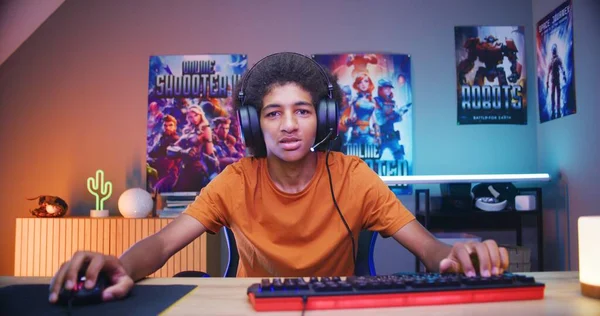 ヘッドフォンでプロのアフリカ系アメリカ人の十代のゲーマーはマイクに話し 居心地の良いネオンルームでコンピュータ上でオンラインビデオゲームをプレイします Esportsトーナメント 自宅でゲーム Pc画面の視点からの眺め — ストック写真