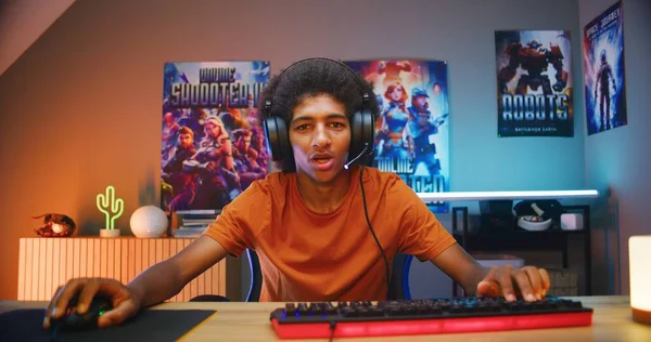 专业的非洲裔美国青少年游戏玩家在耳机里对着麦克风说话 在舒适的霓虹灯房间里在电脑上玩网络游戏 Esports锦标赛 在家里玩游戏 从电脑屏幕的角度来看 — 图库照片