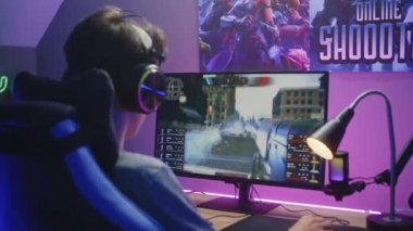 Kulaklıklı genç oyuncu bilgisayarda birinci şahıs nişancıyla oynuyor. Çevrimiçi video oyunu canlı yayın veya siber spor şampiyonluğu. Masa, RGB LED lambasıyla aydınlatılmış. Evde oyun oynuyordum. Dolly vurdu..