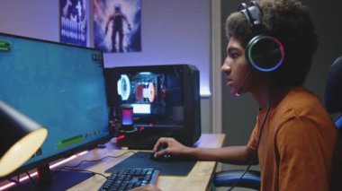 Profesyonel eSports Afro-Amerikalı, kulaklıklı genç oyuncu son model neon odasındaki bilgisayar ekranında çevrimiçi olarak üçüncü şahıs 3D nişancı olarak oynuyor ve kazanıyor. Video oyunu canlı yayın veya siber spor yarışması.