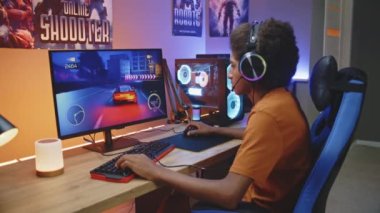 Afro-Amerikalı bir adam, kulaklıklı genç bir oyuncu neon kaplı odada modern güçlü PC 'de çevrimiçi 3D yarış oyunu oynuyor. Video oyunu canlı ya da profesyonel eSports turnuvası. Evde oyun oynamak..