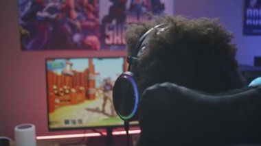 Profesyonel Afro-Amerikalı kulaklıklı genç oyuncu, siber oyun neon odasında modern bilgisayarda üçüncü şahıs 3D nişancı oynuyor. PVP video oyunu canlı yayında ya da eSports turnuvasında. Arka plan.