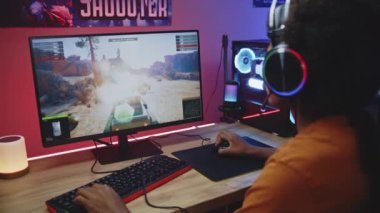 Kulaklıklı Afrikalı Amerikalı genç oyuncu neon odasındaki güçlü kişisel bilgisayarda online tank savaşı veriyor. Video oyunu canlı ya da profesyonel eSports turnuvası. Evde oyun oynamak..