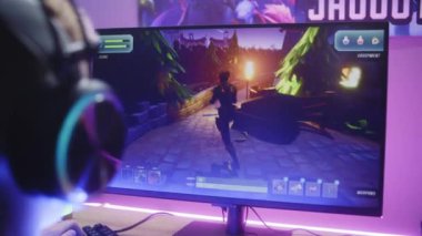 Kulaklıklı çocuk üçüncü şahıs nişancıyı oynuyor. Oyuncu ev bilgisayarında online video oyunu oynamayı seviyor. Masa, RGB LED lambasıyla aydınlatılmış. Evde oyun oynama kavramı. Arkadan bak. Kapat..