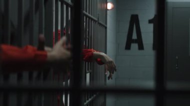 Turuncu üniformalı mahkumlar hapishane hücrelerindeki metal parmaklıklara yaslanıyor. Suçlu suçlular, hapishanede ve gözaltı merkezinde işledikleri suçlardan hapis cezalarına çarptırıldılar. Yaşlı mahkum agresif bir şekilde konuşur. Hücreden görüntüle