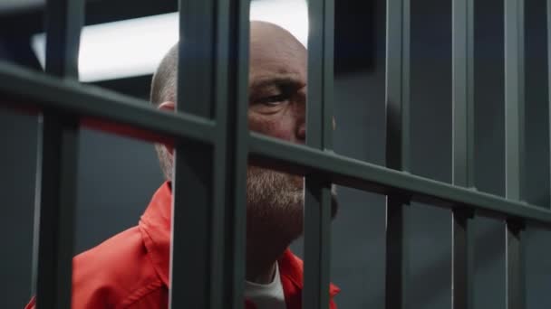 Zbliżenie Starszego Więźnia Pomarańczowym Mundurze Stojącego Metalowymi Kratami Celi Winny — Wideo stockowe