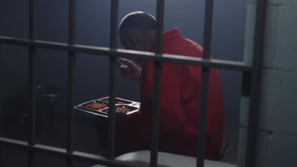 オレンジの制服を着た高齢の囚人は刑務所の独房に座り 夕食を食べる 犯罪者 被収容者は 懲役刑を言い渡される 刑務所 拘置所又は矯正施設 金属製の棒で撃つ — ストック動画