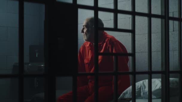身穿橙色制服的老罪犯坐在监狱的床上 想着自由 抑郁的囚犯在监狱里服刑 拘留中心或教养所的有罪囚犯 — 图库视频影像