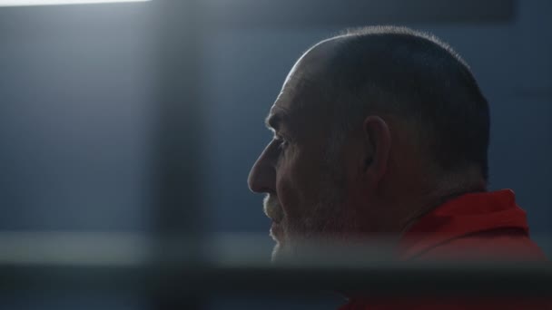 Turuncu Üniformalı Yaşlı Suçlu Hücrede Oturur Parmaklıklı Pencereye Bakar Gözaltı — Stok video