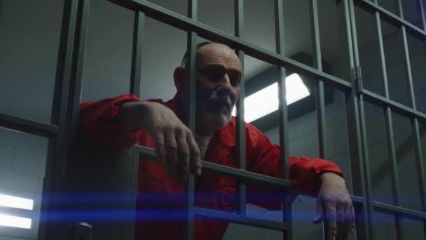 Пожилой Заключенный Оранжевой Форме Держит Руках Металлические Прутья Тюрьме Виновный — стоковое видео