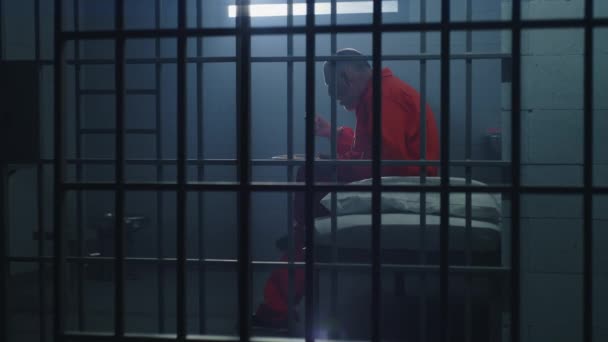Starszy Więzień Więzień Pomarańczowym Mundurze Siedzi Celi Jedzenie Przestępca Odsiaduje — Wideo stockowe