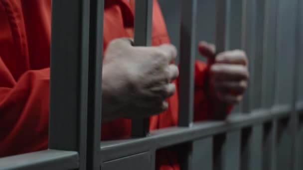 手紧紧抓住身穿橙色制服的老年囚犯 手里拿着金属棒 站在监牢里 罪犯因犯罪而服刑 在监狱或教养所的囚犯 司法系统 — 图库视频影像
