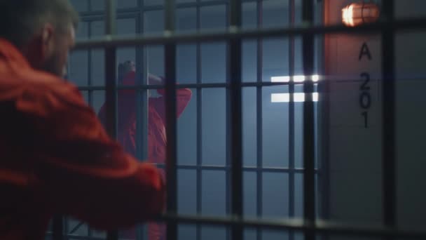 Mężczyzna Pomarańczowym Mundurze Stoi Celi Trzyma Ręce Kraty Więzień Sąsiada — Wideo stockowe