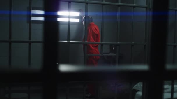 身穿橙色制服的老年囚犯站在那里 走进监牢 把手放在铁棍上 看着镜头 罪犯在监狱 拘留中心或教养所服刑 — 图库视频影像