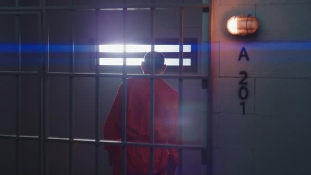 身穿橙色制服的老罪犯坐在监牢里 站起来 用铁棍看着窗户 在拘留中心或教养所的有罪囚犯 犯人将被监禁 — 图库视频影像