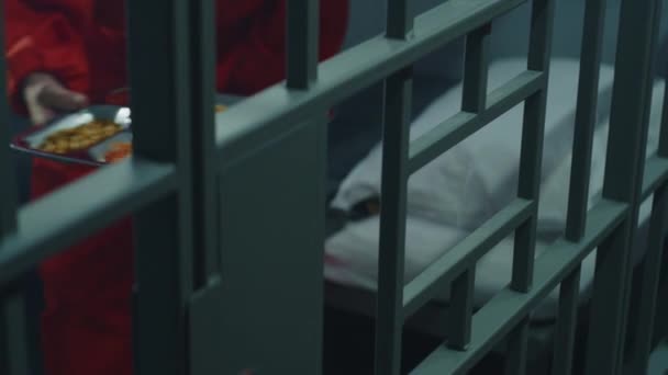 关闭监狱长办公室 通过金属栅栏向囚犯提供一盘食物 身穿橙色制服的老年囚犯坐在监牢里吃饭 在监狱或拘留中心服刑 — 图库视频影像