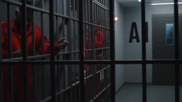 身穿橙色制服的囚犯把铁棍关在监狱里 有罪的罪犯在监狱中服刑 在拘留中心或教养所的愤怒囚犯 从监牢里看 — 图库视频影像