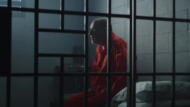 身穿橙色制服的老罪犯坐在监狱床上 与狱友交谈 沮丧的囚犯在监狱里服刑 拘留中心或教养所的有罪囚犯 — 图库视频影像