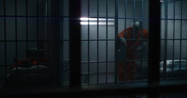 Turuncu üniformalı yaşlı suçlu parmaklıklara yaslanıyor ve hapiste komşusuyla konuşuyor. Islah evindeki ya da ıslah evindeki suçlu mahkumlar. Kasvetli mahkumlar hapis cezasına çarptırıldı..