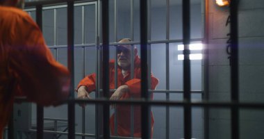 İki suçlu hapiste birlikte hapis cezasına çarptırıldı. Yaşlı suçlu hücrede duruyor, parmaklıkların üzerinde el ele tutuşuyor ve komşusuyla konuşuyor. Gözaltı merkezinde ya da cezaevinde saldırganlar.