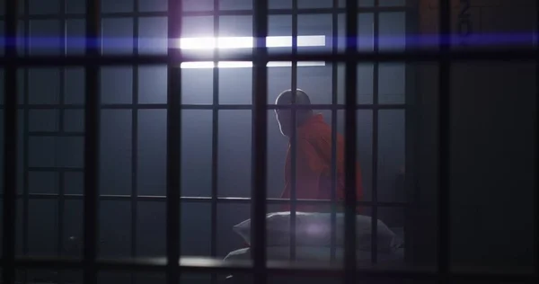 オレンジの制服を着た高齢の犯罪者が刑務所の独房に座って立ち上がり バーのある窓を見ている 拘置所又は矯正施設における有罪の被収容者 囚人は刑期を務める — ストック写真