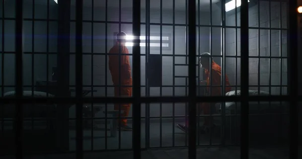 収容所又は矯正施設に収容されている2人の受刑者 オレンジの制服を着た高齢犯罪者が刑務所のベッドに座り セルメイトと話をする 囚人は独房で懲役刑を言い渡される — ストック写真