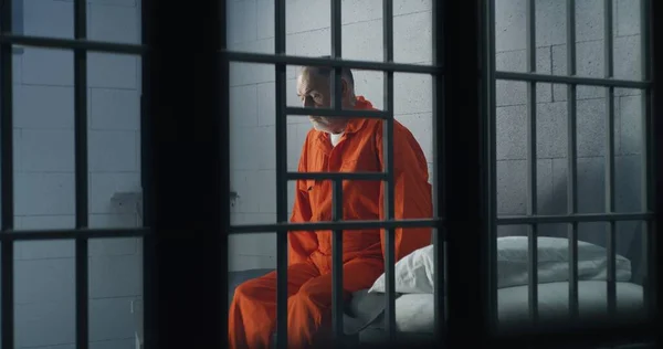 オレンジの制服を着た高齢犯罪者が刑務所のベッドに座り 自由を考えています 囚人は独房で懲役刑を言い渡される 拘置所又は矯正施設における有罪の被収容者 — ストック写真
