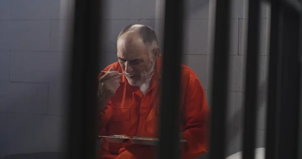 Der Gefängniszelle Sitzt Ein Älterer Häftling Orangefarbener Uniform Gefängniswärter Reicht — Stockfoto