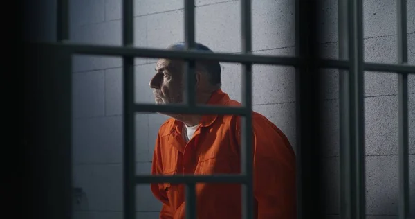 オレンジの制服を着た高齢犯罪者が刑務所のベッドに座り 自由を考えています 囚人は独房で懲役刑を言い渡される 拘置所又は矯正施設における有罪の被収容者 — ストック写真