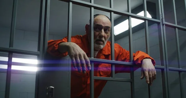 オレンジの制服を着た高齢の囚人は 刑務所の金属棒を手に持っています 有罪の犯罪者は刑務所の独房での犯罪の懲役刑を言い渡される 収容所又は矯正施設の被収容者 — ストック写真